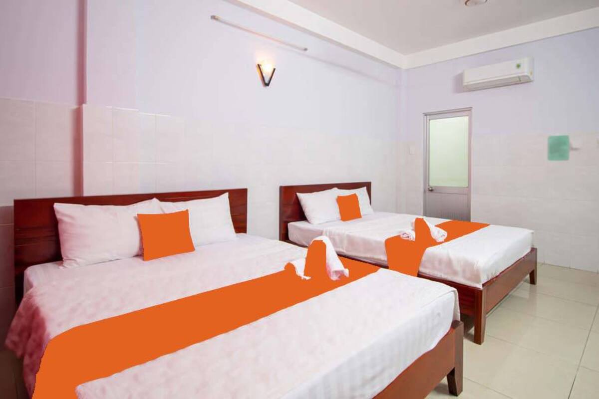 Une chambre d’hôtel avec deux lits, du linge de lit blanc, des touches de couleur orange, un climatiseur fixé au mur et une porte en verre dépoli.