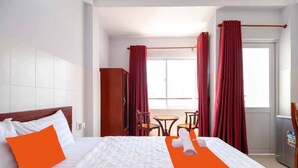 Ein Hotelzimmer mit Bett, Schreibtisch und Stuhl. Vor den Fenstern hängen Vorhänge.