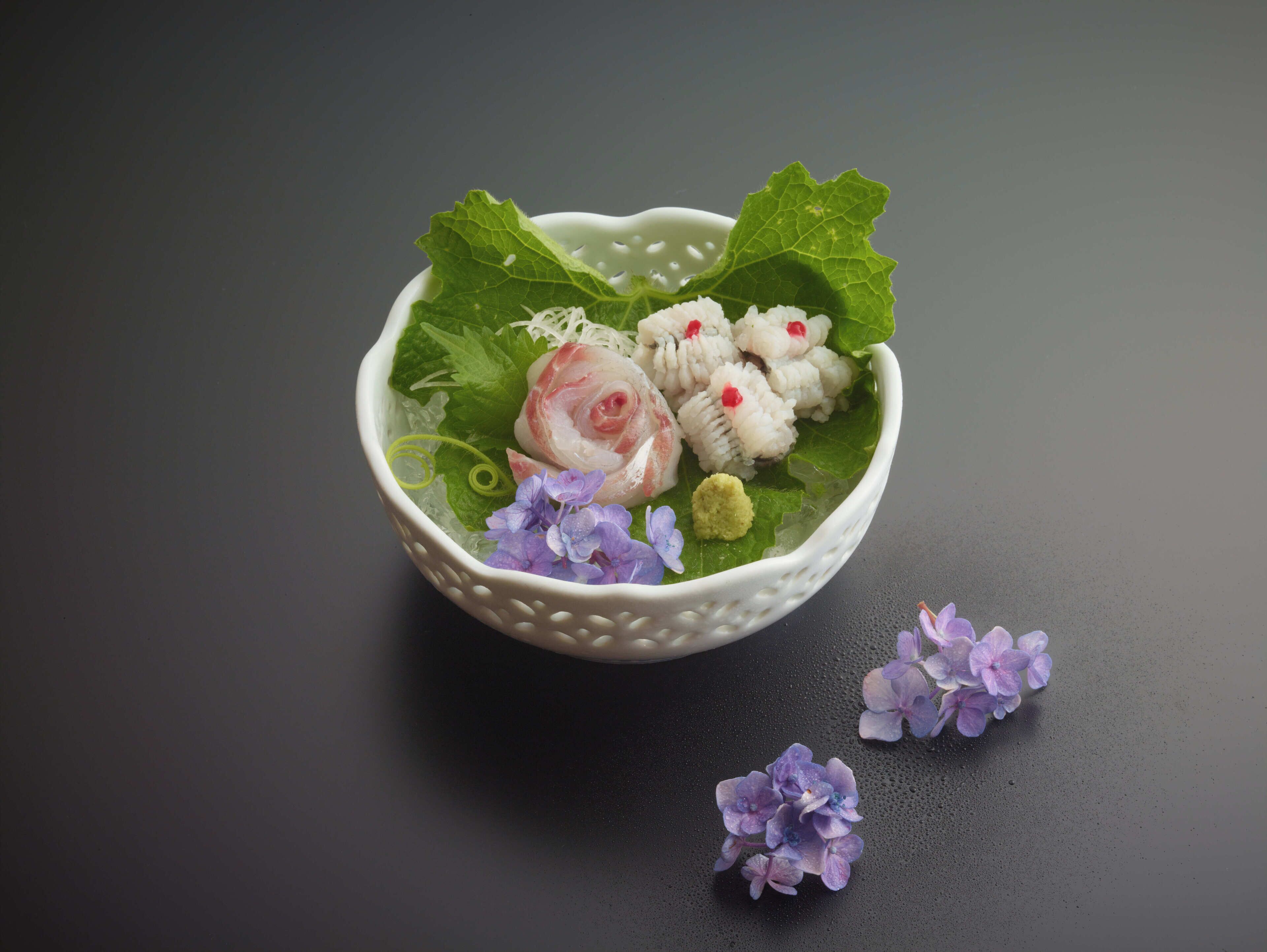 A bowl with food and flowers on a dark surface.
