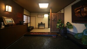 Een traditioneel Japans interieur met een receptiebalie, een kleine tafel met een theepot, een houten bank en een grote potplant.