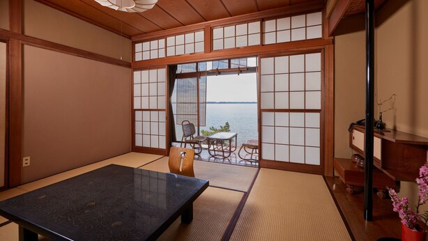Een traditionele Japanse kamer met tatami vloerbedekking, een lage tafel, een bank en uitzicht op zee door shoji schermen.
