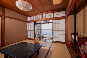 A traditional Japanese room with tatami flooring, a low table, a sofa, and a view of the sea through shoji screens. - Ryokan Kinsui (Hamamatsu)