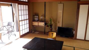 A traditional Japanese room with tatami flooring, a low table, a chair, a television, and a sliding door.