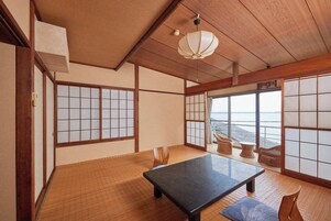 Um quarto japonês tradicional com tatames, biombos shoji, uma mesa baixa e vista para o mar.
