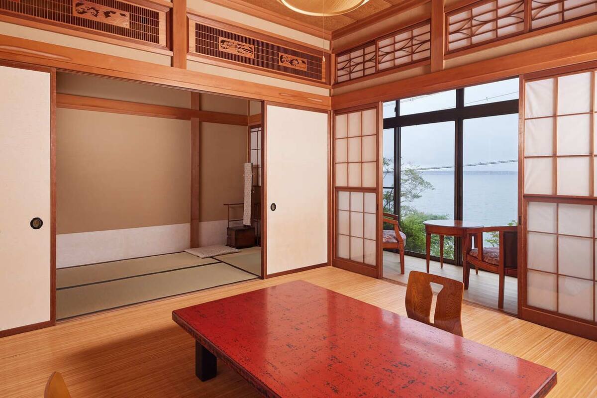 A traditional Japanese room with tatami flooring, sliding doors, a wooden table, and a view of the sea.