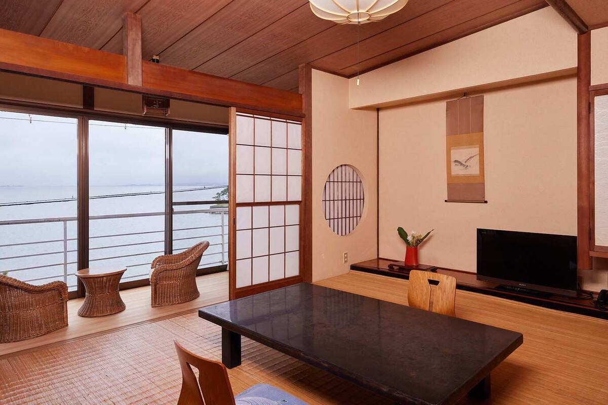 A room with a large window, a flat-screen TV, a wooden table, and traditional Japanese sliding doors.