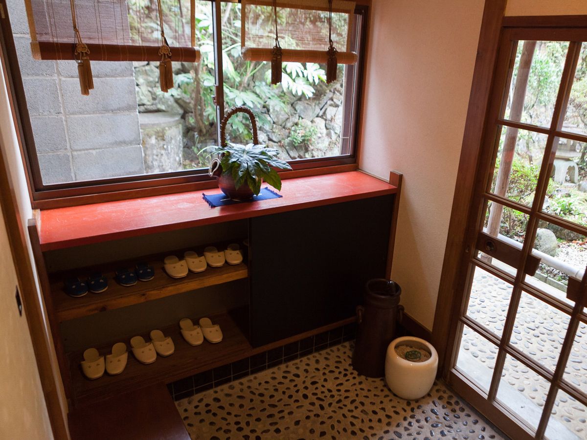Una cocina pequeña con ventana, un estante con zapatos y una planta en maceta.