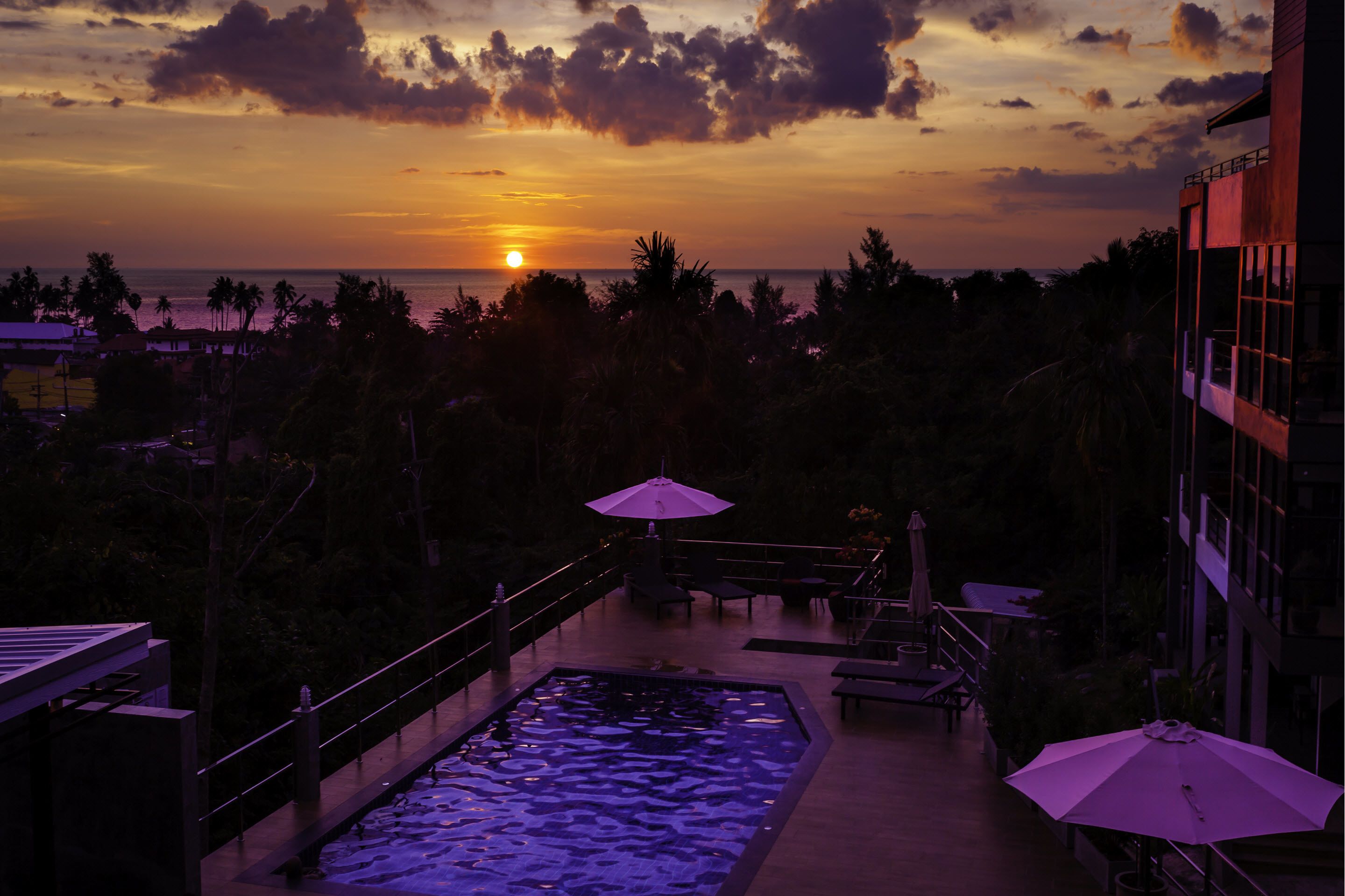 A pool area with a sunset view, outdoor seating, and a building with balconies.