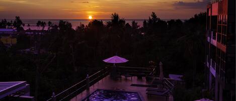 A pool area with a sunset view, outdoor seating, and a building with balconies.