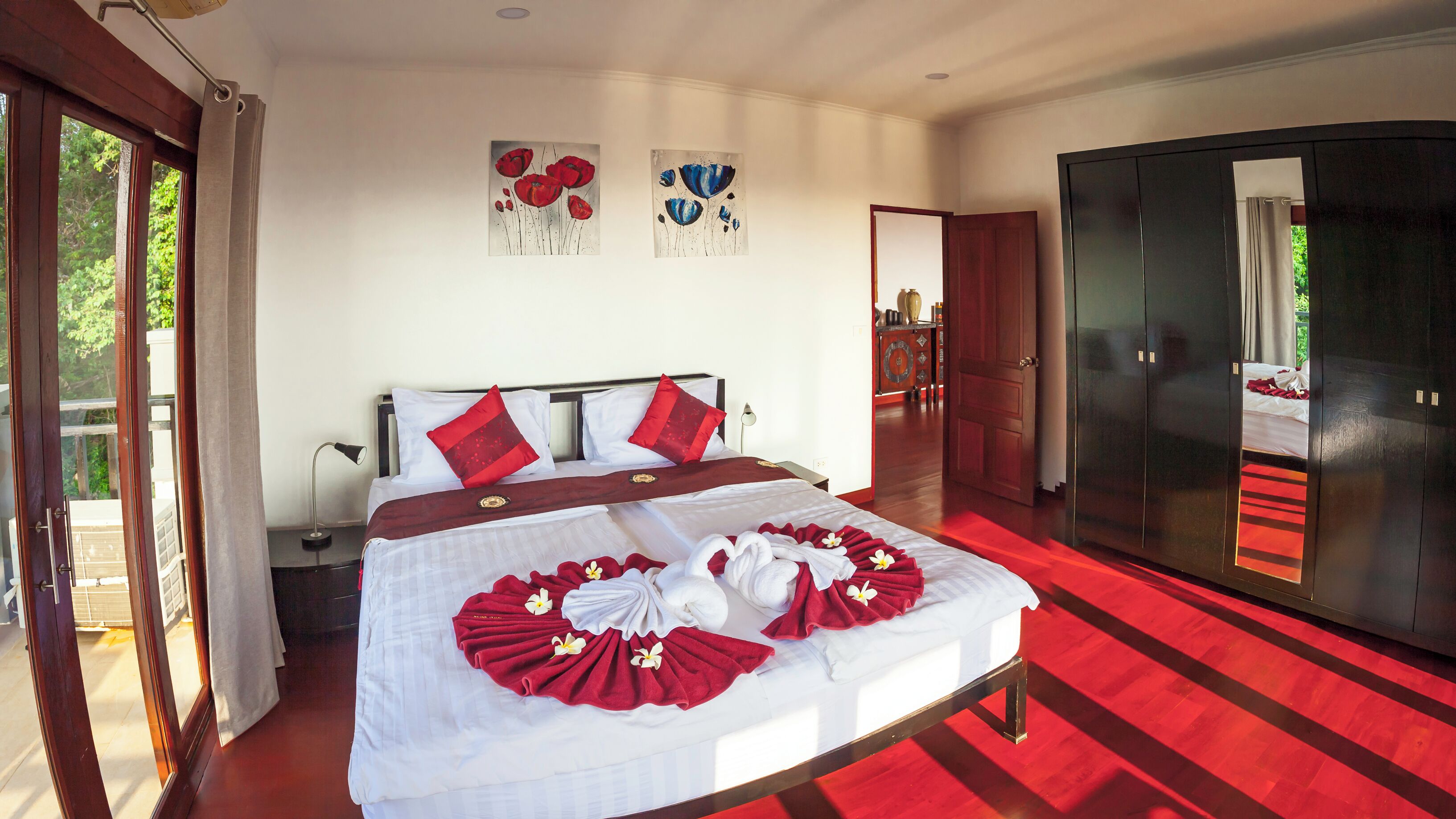 Une chambre d’hôtel avec un grand lit, une literie rouge et blanche, une moquette rouge et des œuvres d’art accrochées aux murs.