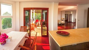 A modern kitchen with a large island, a dining area with a table and chairs, and a view of the outdoor balcony.