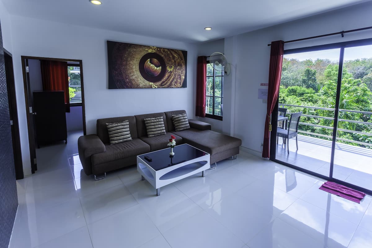 A modern living room with a sofa, a glass coffee table, and a large window with a view of greenery.