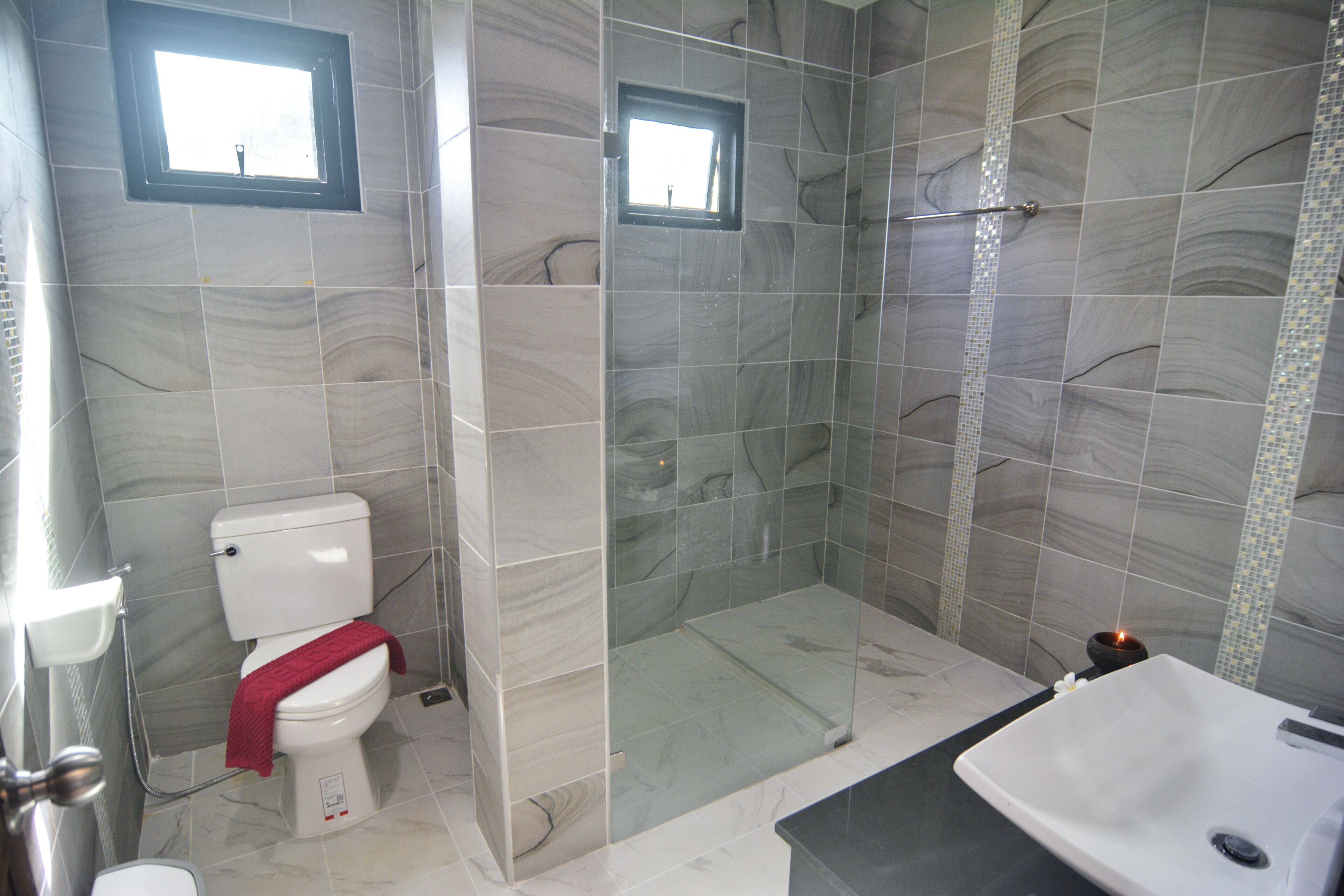 A modern bathroom with a glass-enclosed shower, a toilet with a red towel, and a sink with a black countertop.