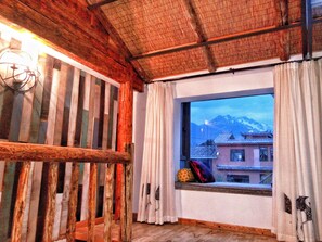 A room with a wooden ceiling, a window with a view of mountains, and a traditional building outside.