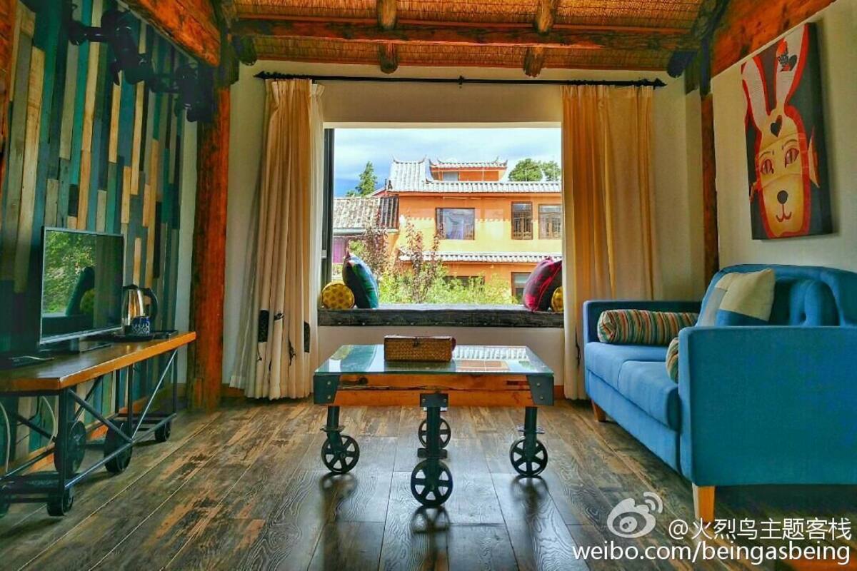 A room with a traditional wooden ceiling and a large window with curtains. There is a blue sofa and a small table with a basket on it.