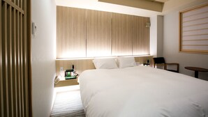 A hotel room with a large bed, wooden headboard, bedside table with a lamp, and a small table with a chair.