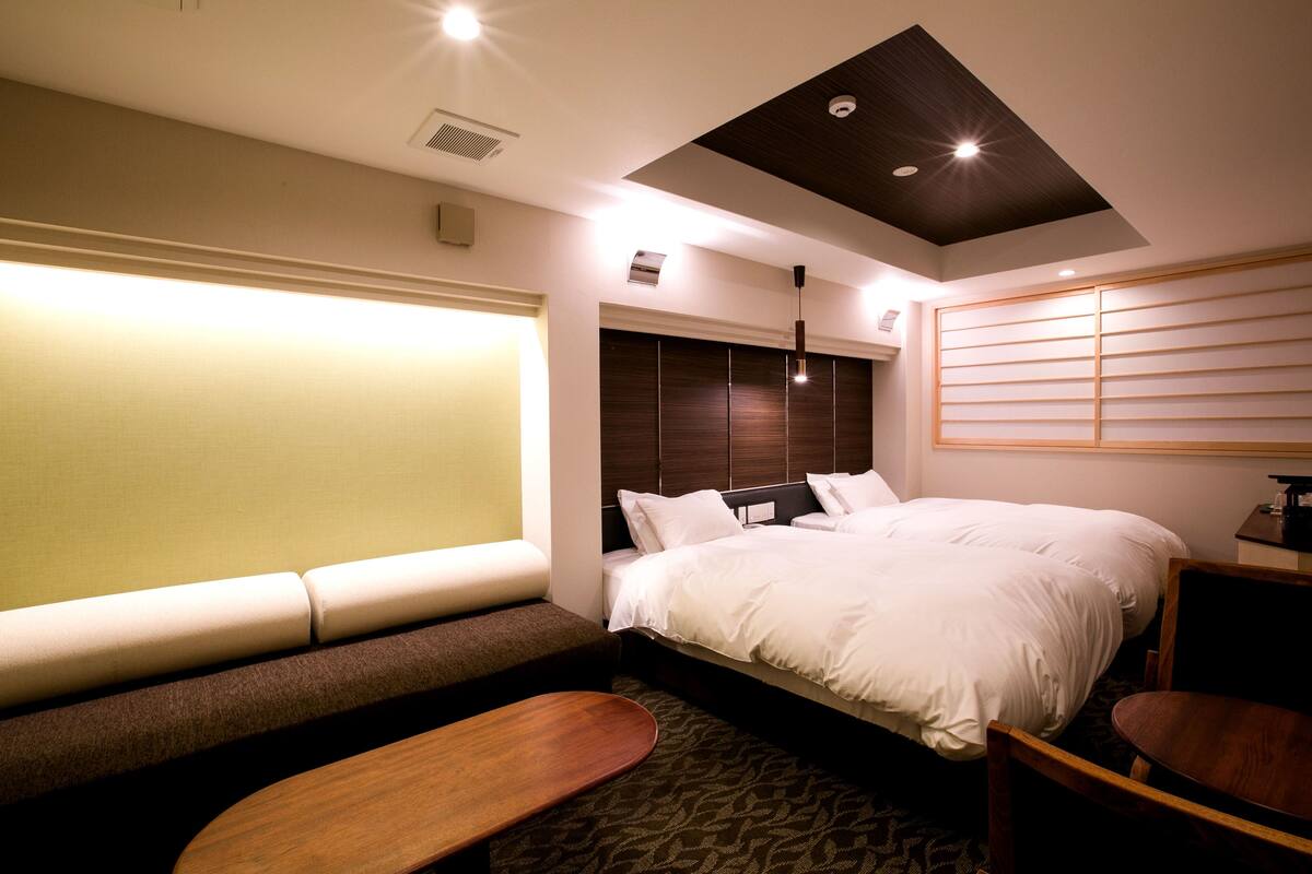 Una habitación de hotel con cama, un banco, un escritorio y una ventana con persianas.