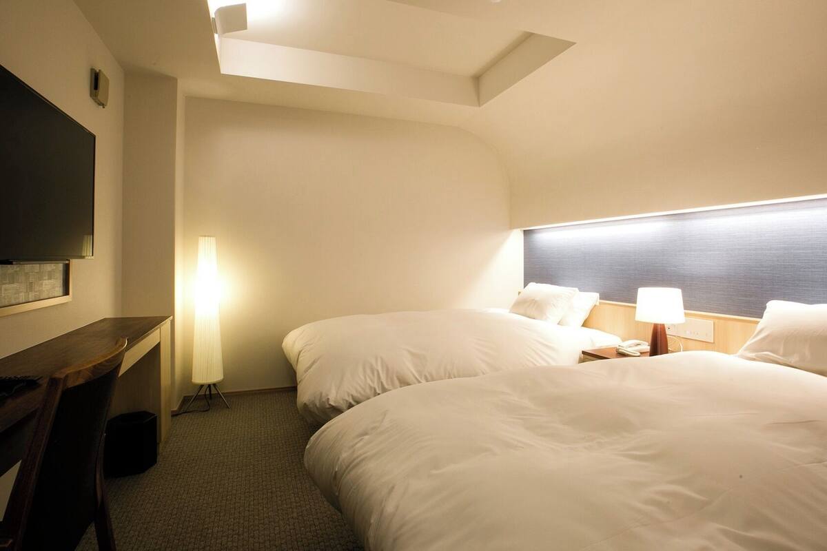 Habitación de hotel con dos camas, un escritorio, un televisor y una lámpara.