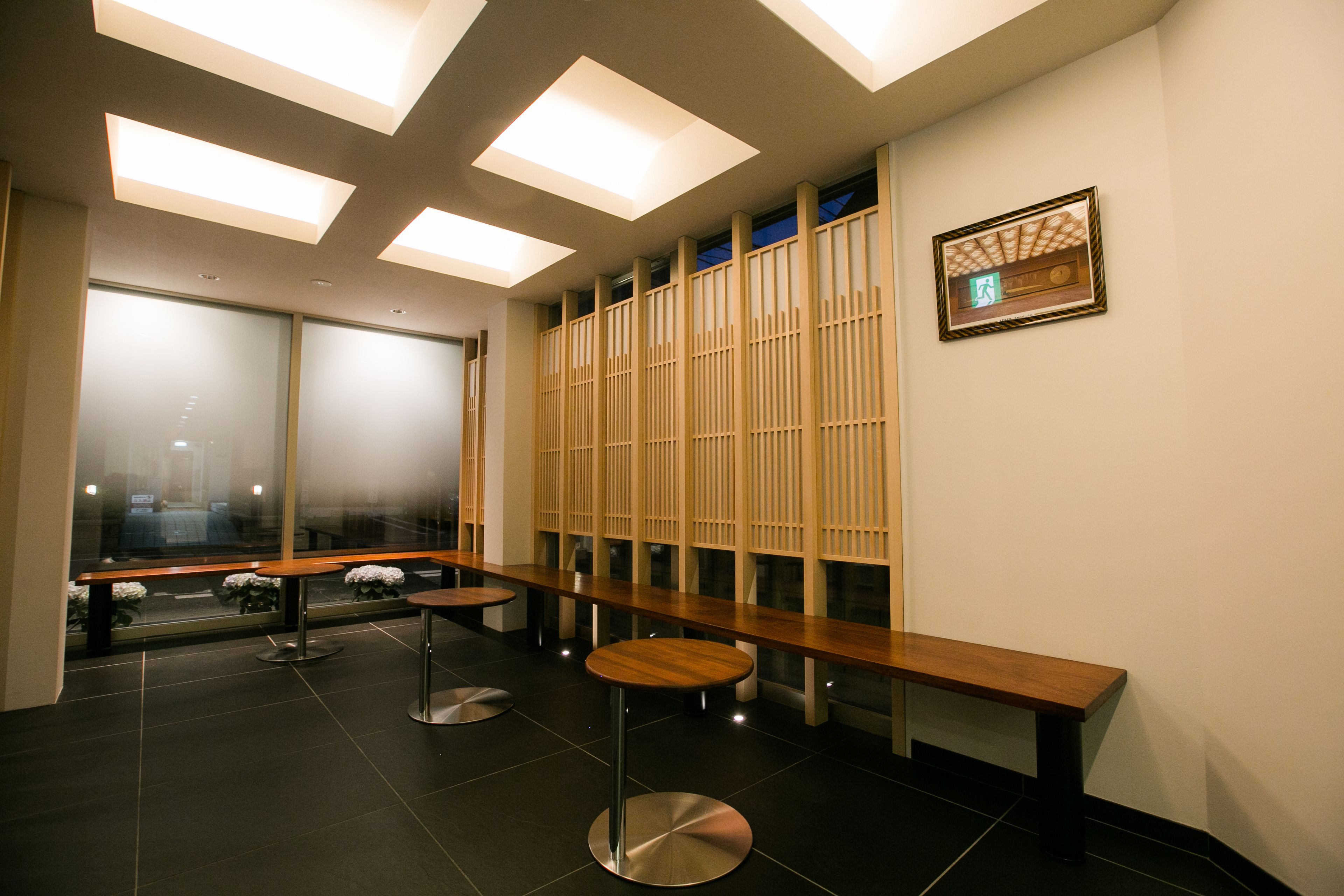 Um interior moderno com um longo banco, mesas redondas e vista através de um painel de vidro.