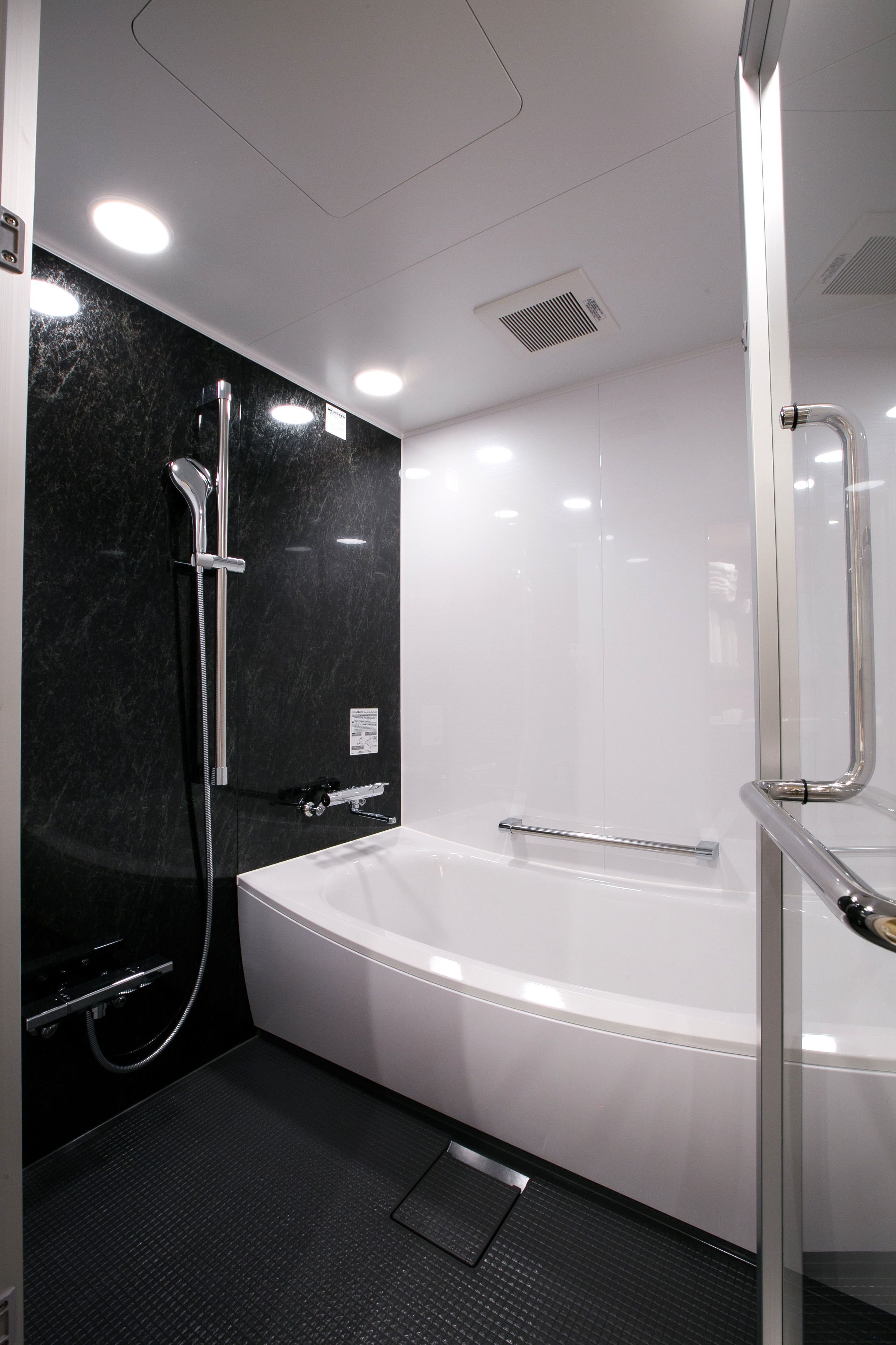 Un baño moderno con pared de mármol negro, una bañera blanca y zona de ducha con mampara de vidrio.