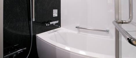 Un baño moderno con pared de mármol negro, una bañera blanca y zona de ducha con mampara de vidrio.
