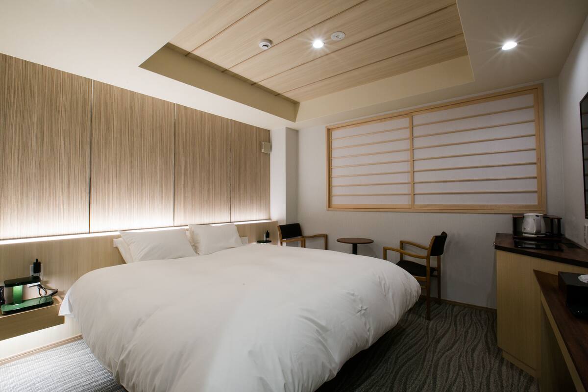 Una habitación de hotel con una cama grande, un escritorio con hervidor, una mesita pequeña y una silla.