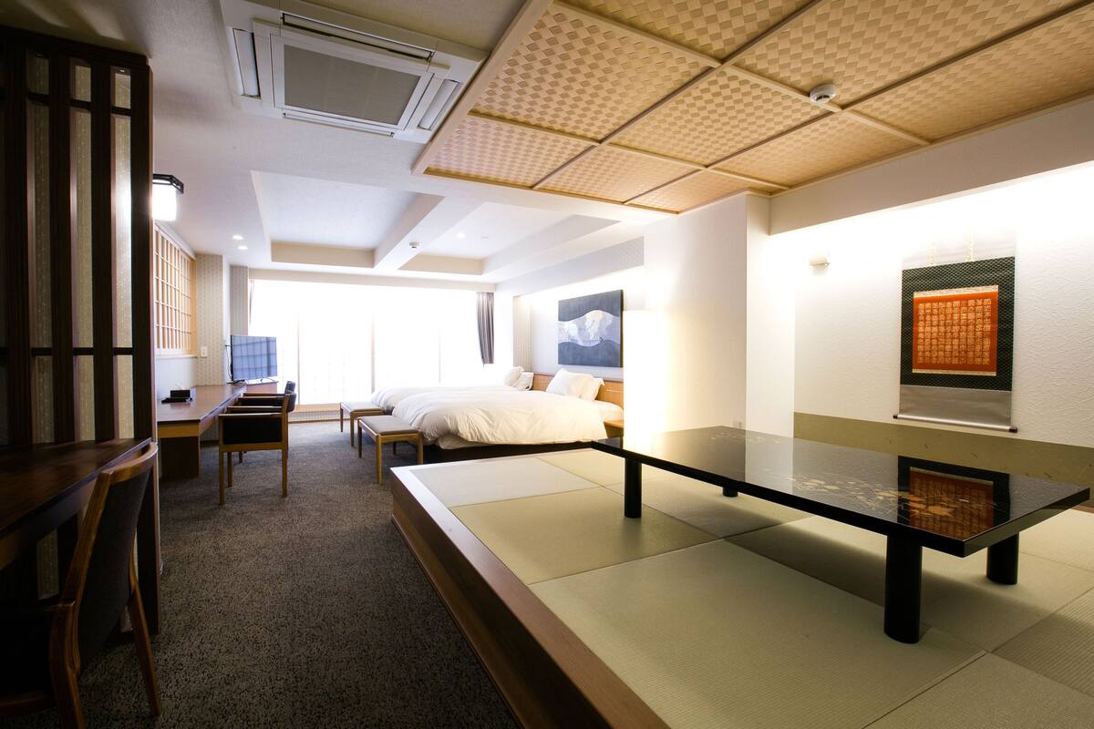 Una habitación de hotel con suelo de tatami, una cama, un escritorio y una silla.