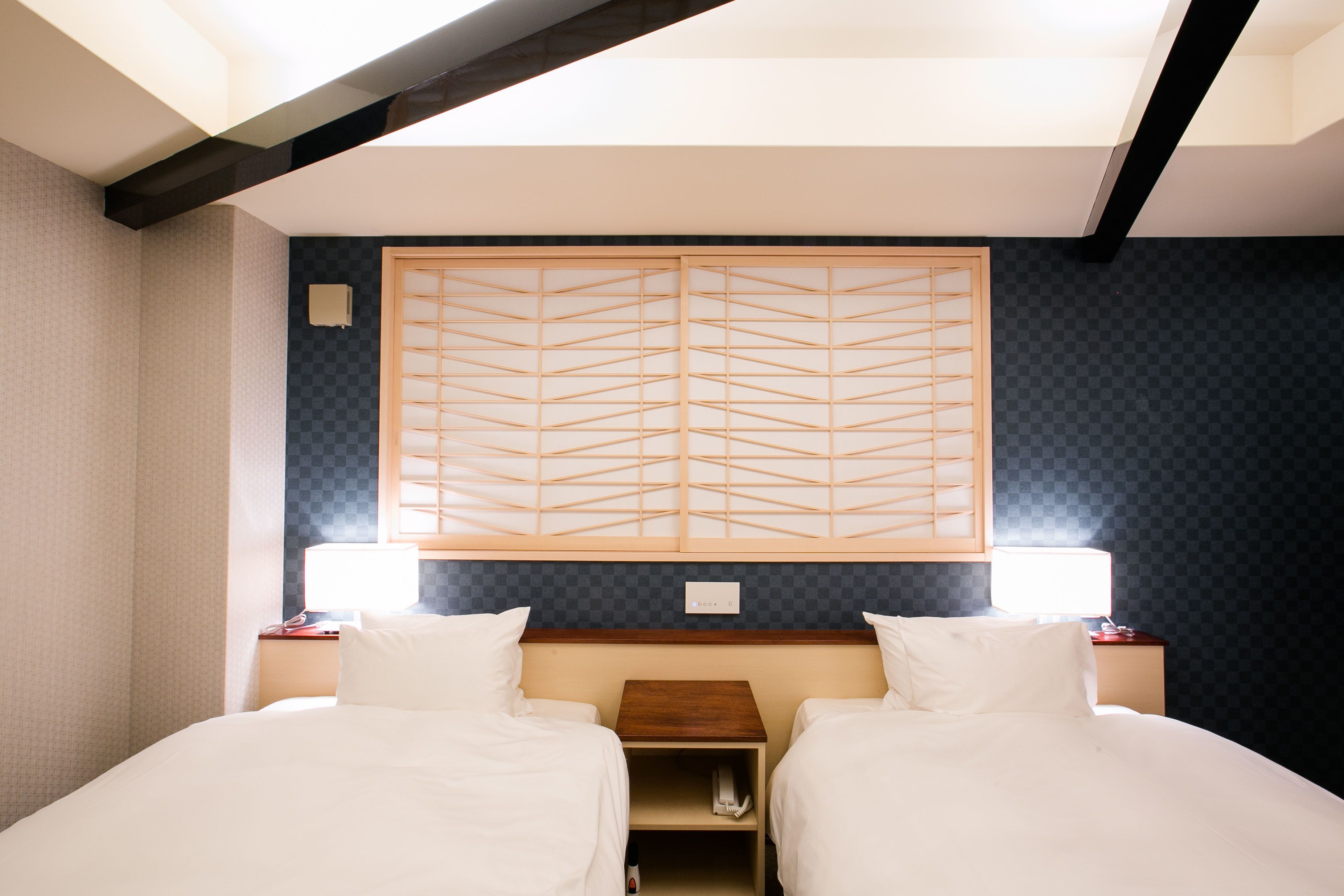 Une chambre d’hôtel avec deux lits, une tête de lit en bois et un motif à carreaux sur le mur.
