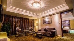 Una habitación de hotel con candelabro, un sofá, dos sillones, una mesa de centro y una planta grande.