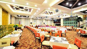 Un salón de banquetes con mesas dispuestas para un evento formal, con alfombra estampada y diseño de techo moderno.