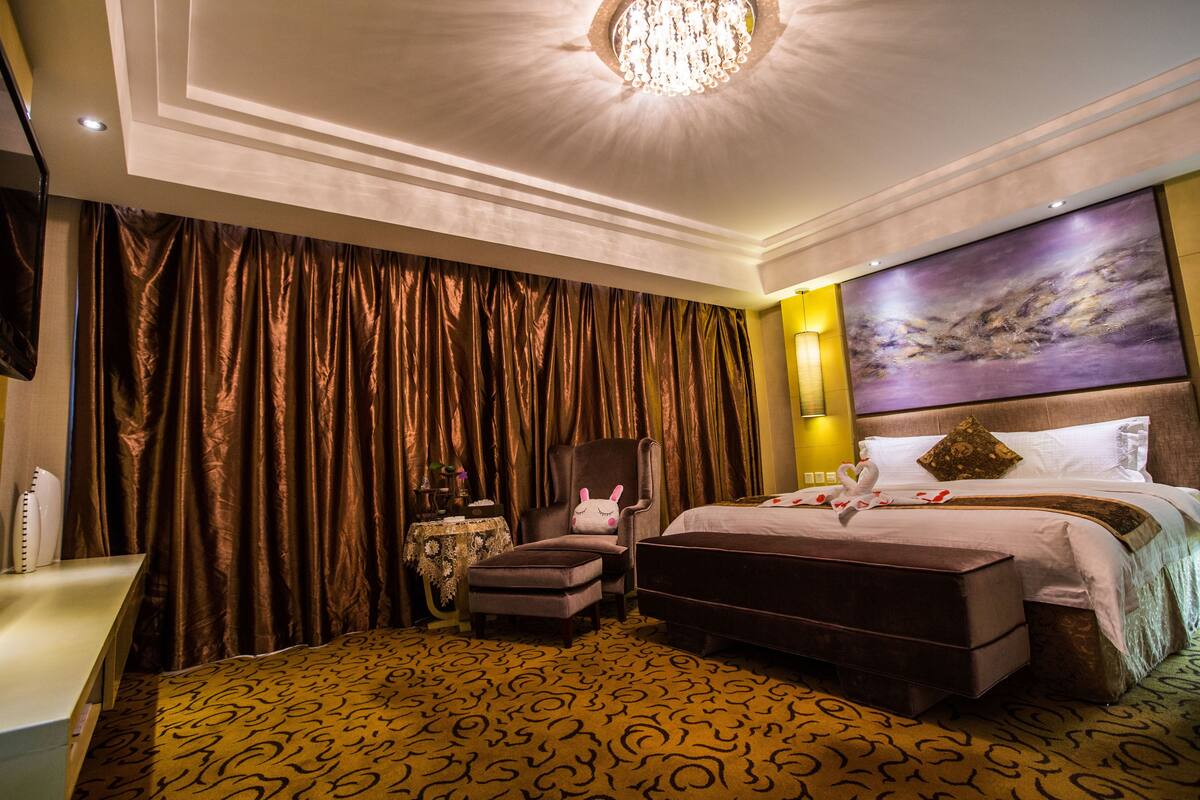 Een hotelkamer met een groot bed, een stoel, een klein tafeltje en een groot schilderij aan de muur.