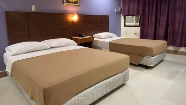 Habitación de hotel con dos camas, una mesita de noche, una lámpara de pared y una ventana con cortinas.