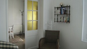 A room with a white door, a bookshelf, a chair, and a radiator. - NORMAN HOUSE IN JUNO BEACH  (Bernières-Sur-Mer)