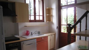 A kitchen with a dishwasher, a sink, and a red oven. There is a window with a view of greenery outside. - NORMAN HOUSE IN JUNO BEACH  (Bernières-Sur-Mer)