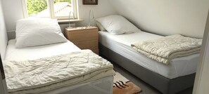 A room with two beds, a bedside table, a nightstand, and a window.