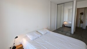 Un dormitorio con una cama, una mesita de noche con lámpara, un espejo y un armario.