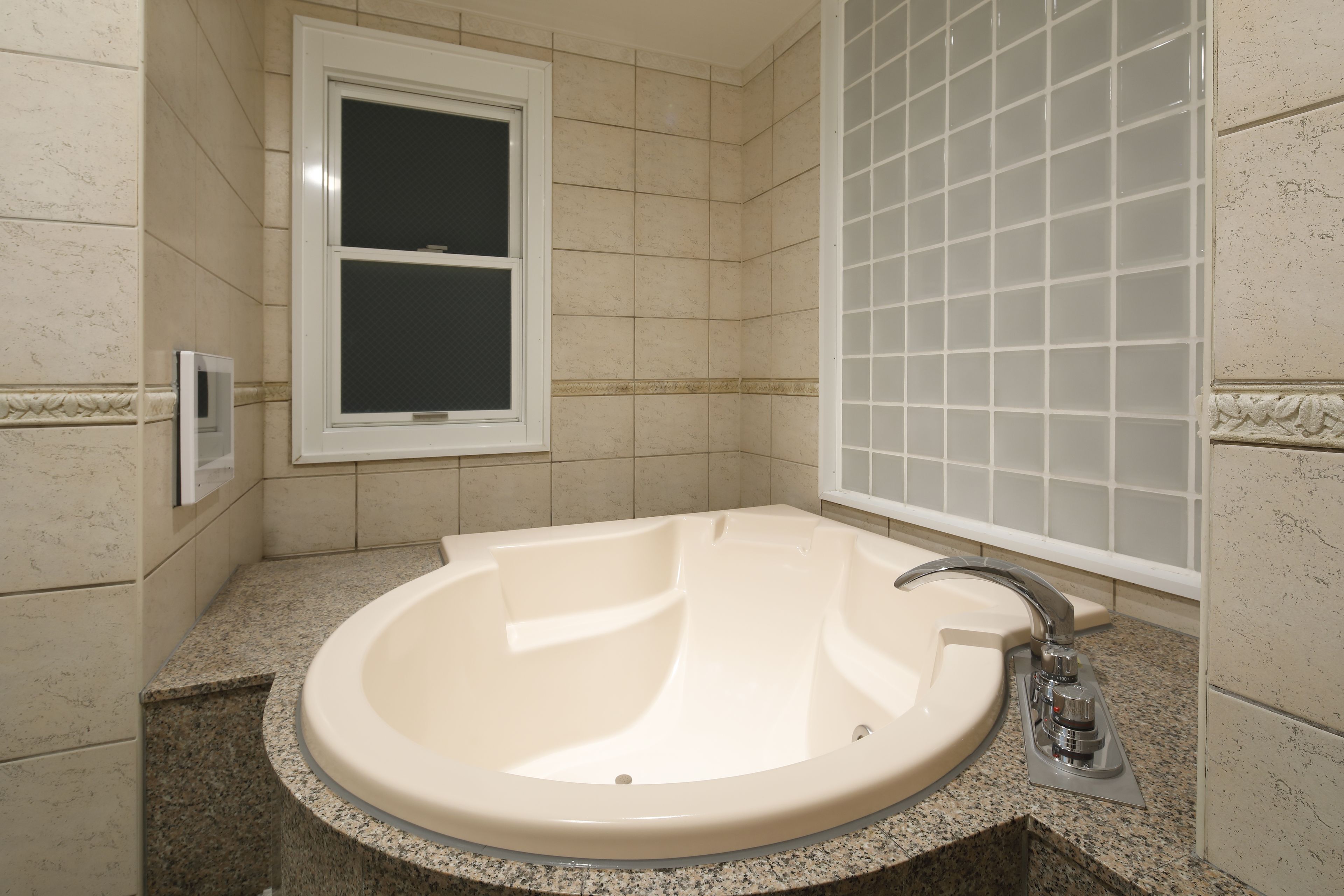 A bathroom with a freestanding bathtub, a window, and tiled walls.