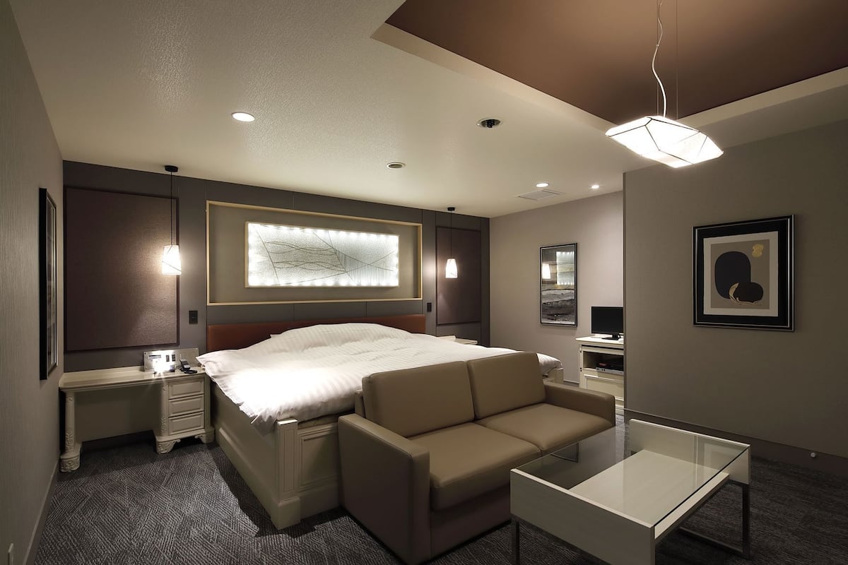 A modern hotel room with a large bed, a sofa, a small table, and a TV.