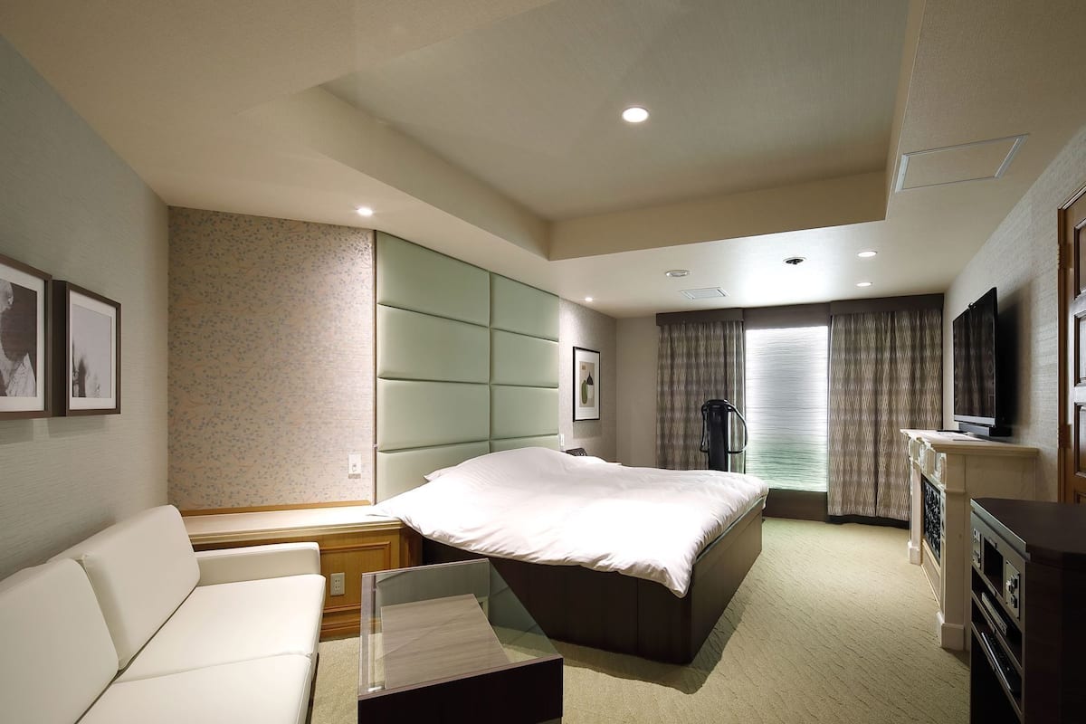 A hotel room with a bed, a sofa, a TV, and a minibar.