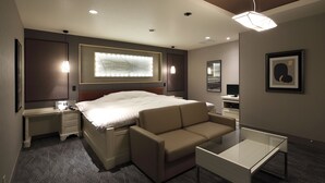 A modern hotel room with a large bed, a sofa, a desk, and a glass table.