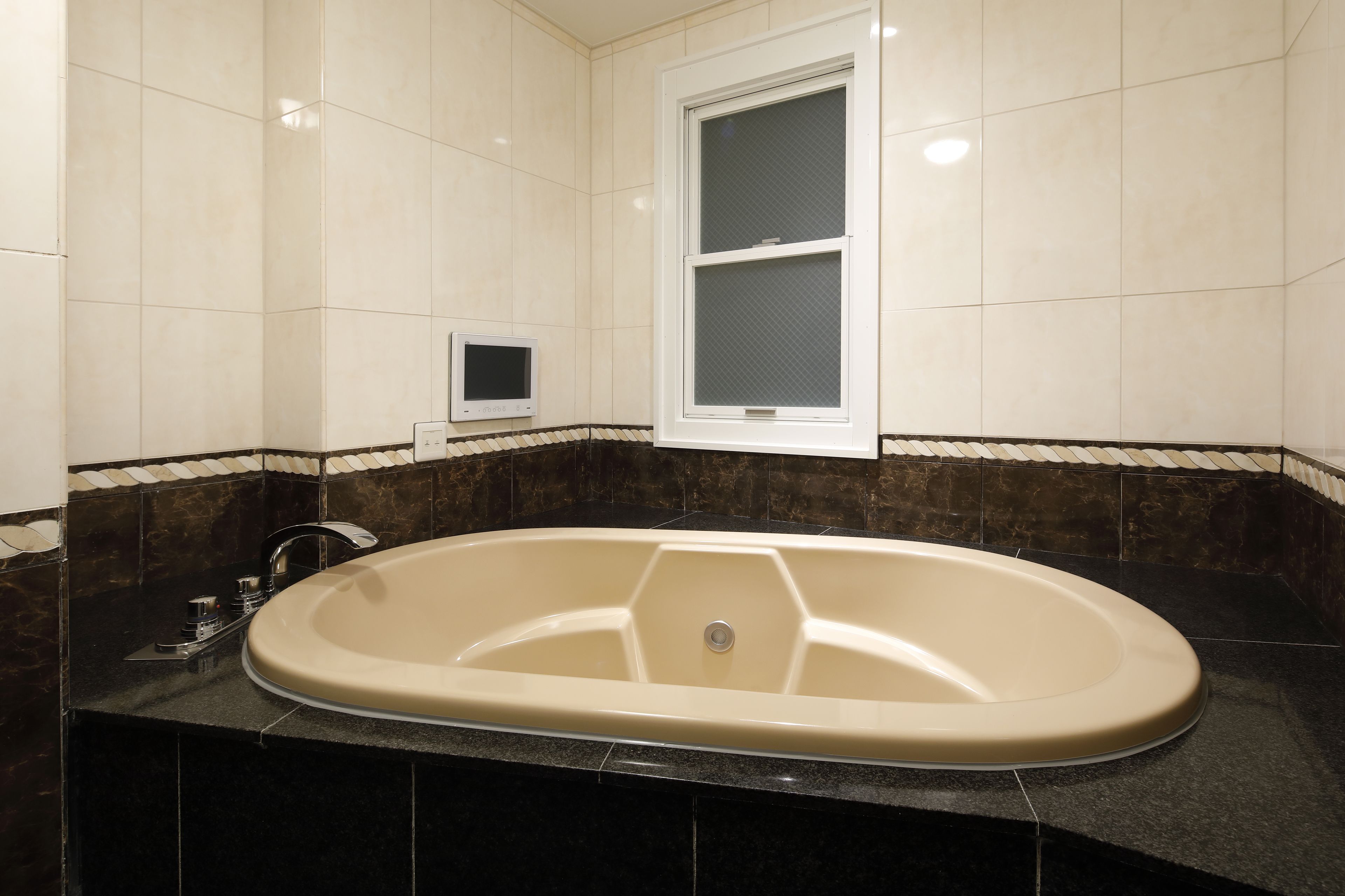 A bathroom with a large bathtub, a window, and a small television on the wall.
