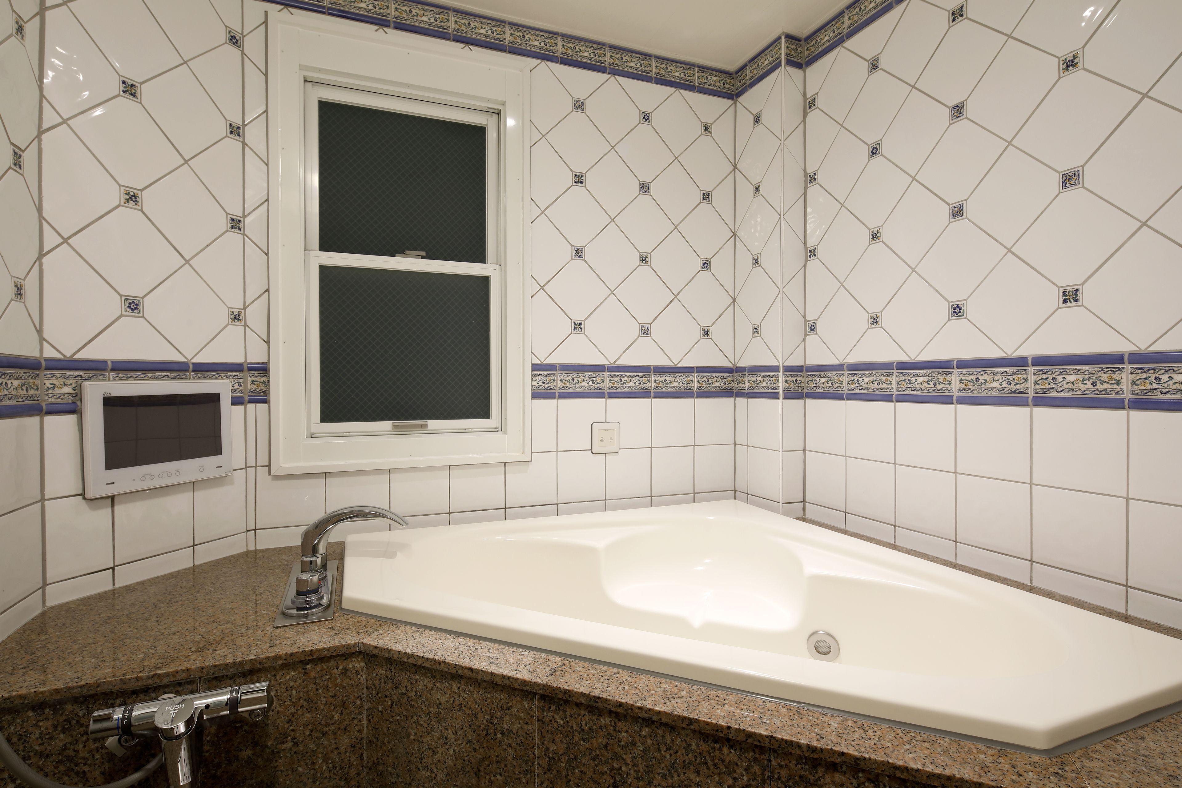 A bathroom with a white bathtub, a window, and a sink with a faucet.