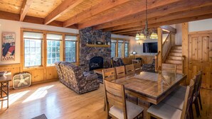 Un vaste espace de vie agrémenté d’une cheminée en pierre, de poutres apparentes en bois et d’une table à manger avec des chaises.