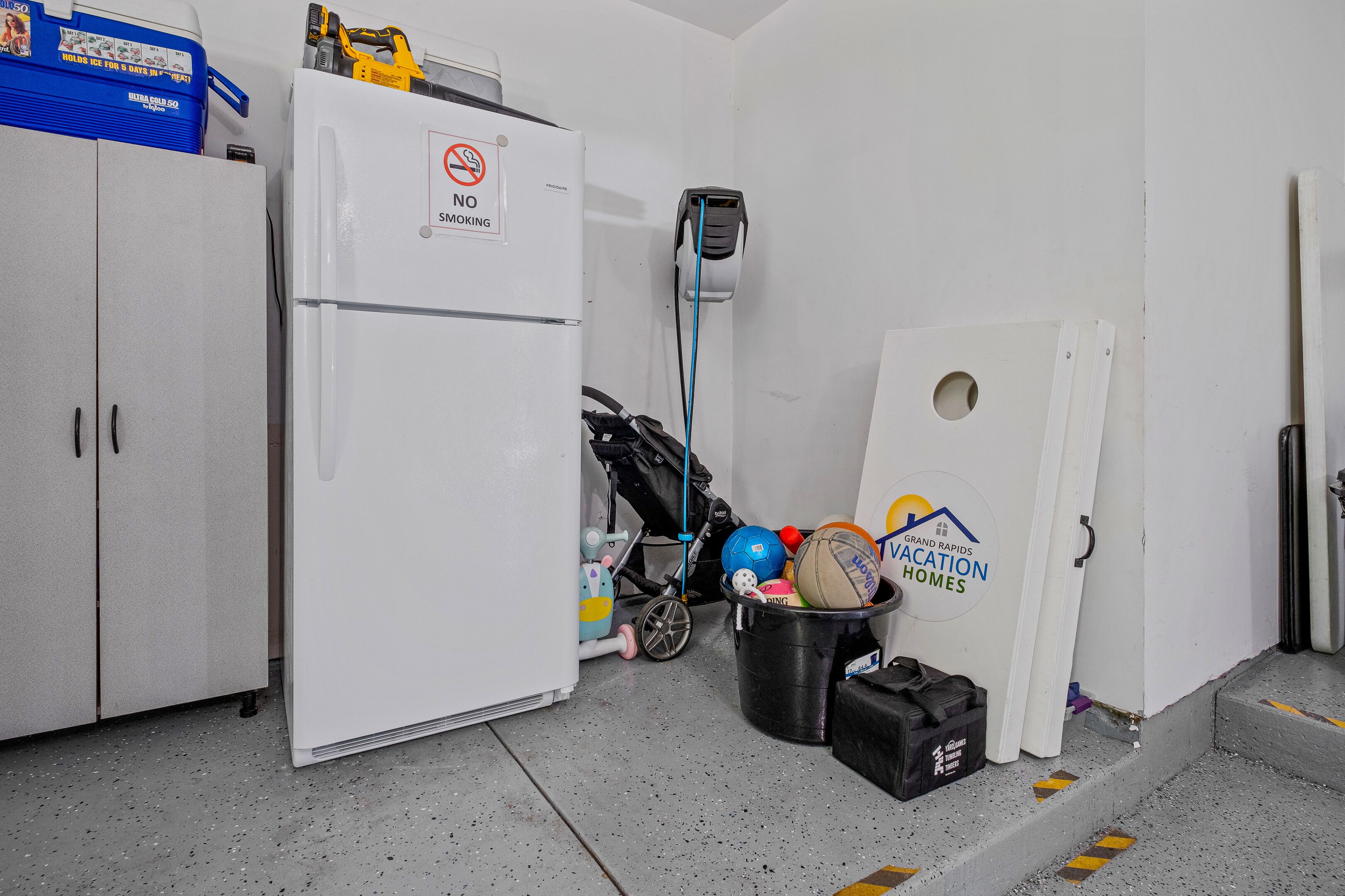 A compact kitchen with a refrigerator, a no smoking sign, a stroller, and a bucket with sports balls.