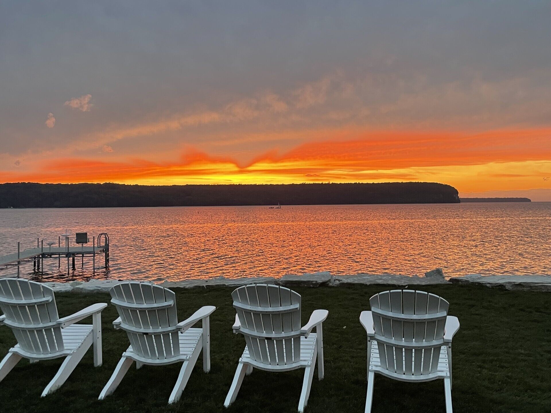 Vista do pôr do sol sobre um lago, com cadeiras na margem.