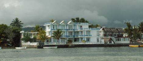 A multi-story hotel with balconies, located near a body of water with boats.