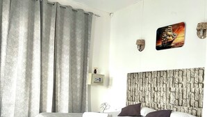 Een netjes ingerichte slaapkamer met een bed, gordijnen, een plafondventilator, een wandklok en een decoratief schilderij van een schip.