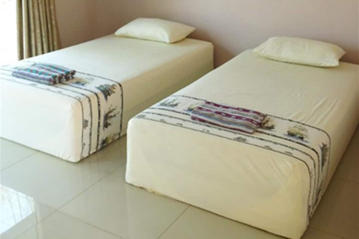 Two single beds with pillows and blankets, a window with curtains, and a tiled floor.