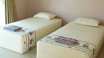 Two single beds with pillows and blankets, a window with curtains, and a tiled floor.