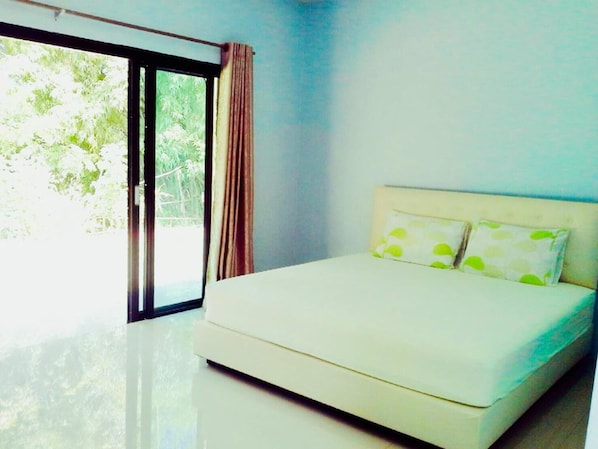 A bedroom with a bed, a window with curtains, and a view of greenery outside.